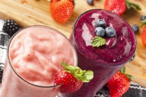 Two fruit smoothies in clear glasses sitting on a wood tabletop