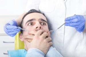 man sitting in dental chair afraid and covering his mouth