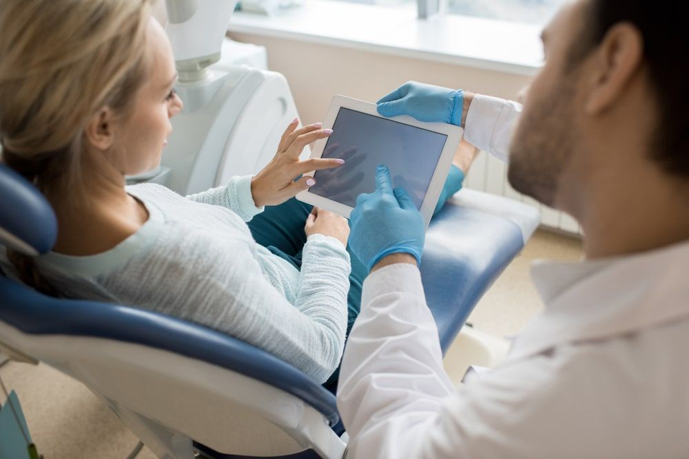 Dentist talking to patient and referencing something on a tablet