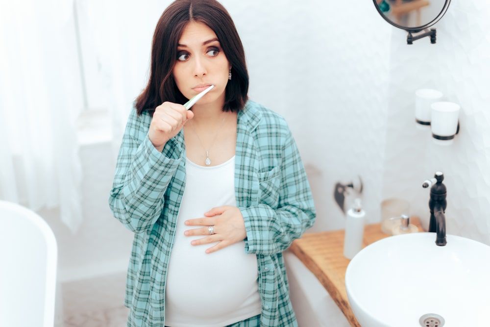 Pregnant Woman Brushing Her Teeth in the Bathroom. Mother o be taking care of oral health during pregnancy