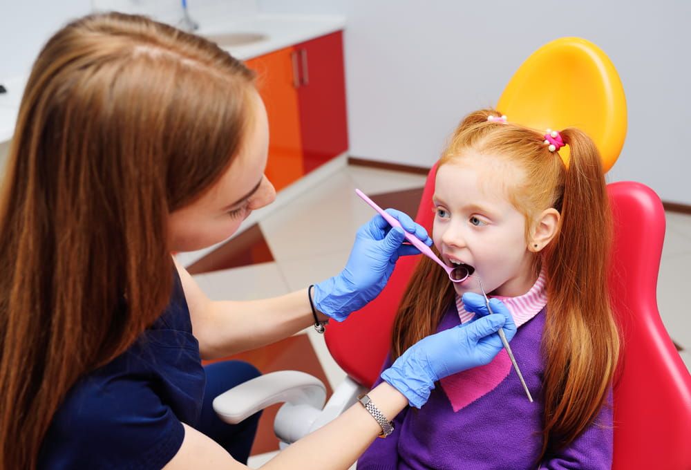 little girl smiling in red dental chair. The dentist examines the teeth of the child's patient. Pediatric dentistry