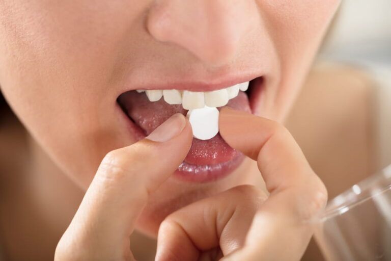 Close-up Of Female Hands Putting One White Round Pill On Tongue