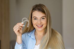 Young woman holding transparent aligners, showing her bright smile,