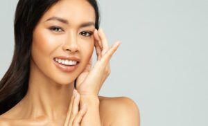 Happy Asian Woman with Perfect White Teeth Smile. Beautiful Chinese Girl applying Eye Cream