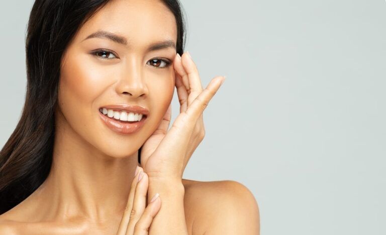 Happy Asian Woman with Perfect White Teeth Smile. Beautiful Chinese Girl applying Eye Cream