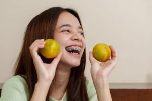 Asian man holding an orange Smiling in a turquoise outfit feel the happiness Bright woman getting braces
