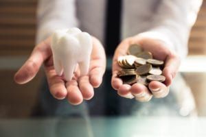 Two hands showing one with a giant tooth and the other with a bunch of coins