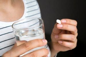 Woman holding a glass of water and a white pill
