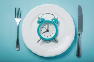 A plate with a blue alarm clock with a fork on one side and a knife on the other side all on a blue background