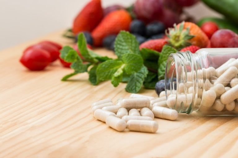 image of vitamins and an assortment of fruits and vegetables on a wooden tabletop