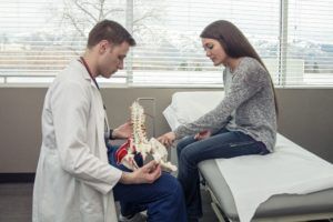 Male doctor showing female patient a model of the spine to demonstrate postoperative care