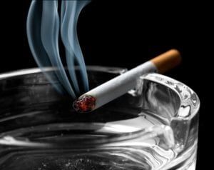 Smoking cigarette hovering over an ashtray on a black background