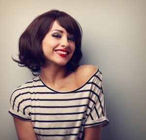 Woman in striped shirt smiling against a gray wall