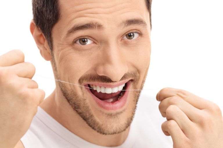 Smiling man having a good time while easily flossing his teeth
