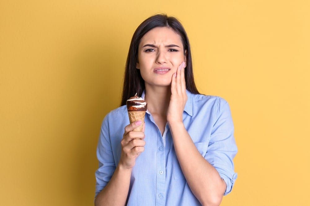 Woman eating an ice cream cone and cringing because her teeth hurt