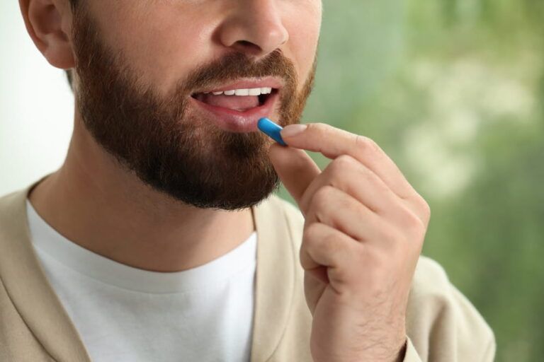 Closeup view of bearded man taking pill on blurred background