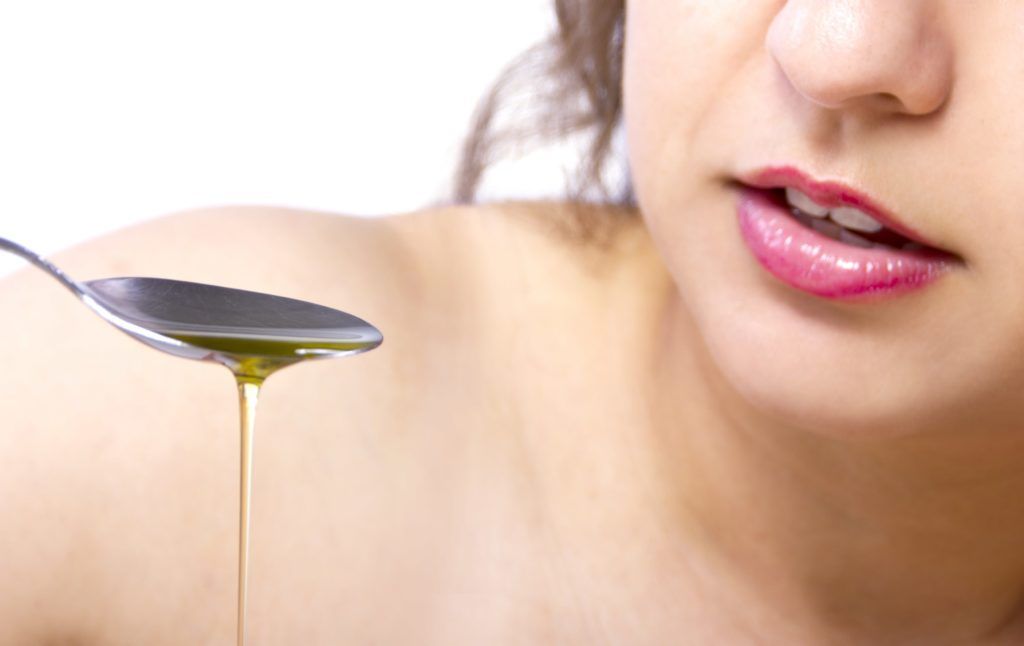 Close up of a woman's mouth and a spoonful of oil
