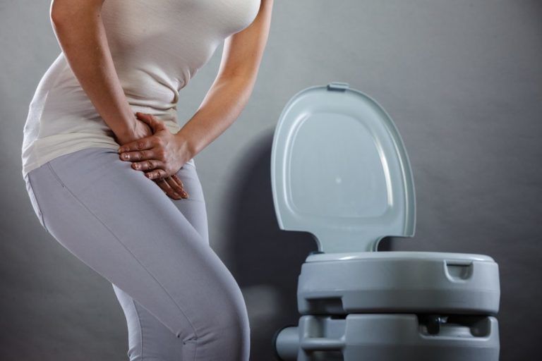 Woman suffering from Urinary Incontinence holding her lower abdomen in front of a toilet