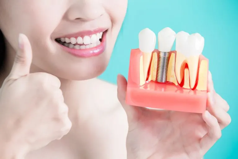 Smiling patient with dental implant in hand