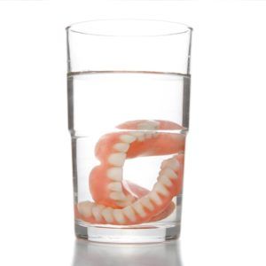 Image of dentures, fake teeth, sitting in a glass of clear water on a white background