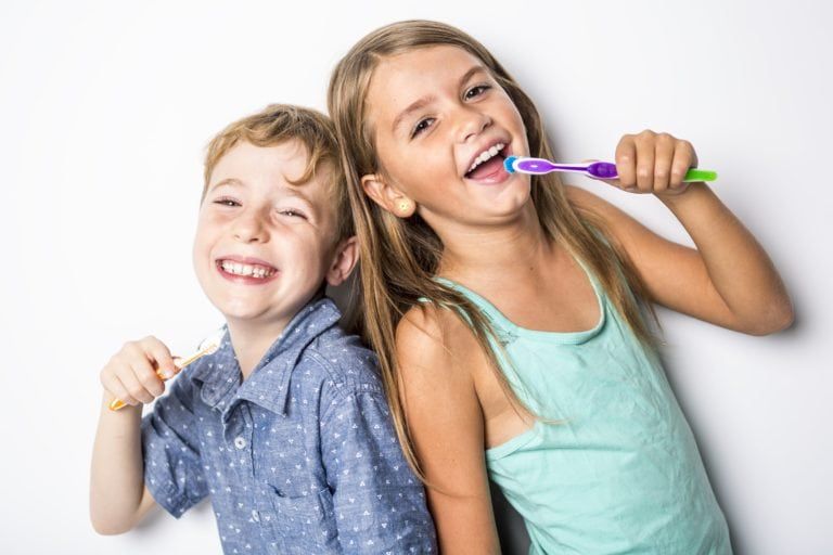 Brother and sister brushing their teeth back to back on a white background