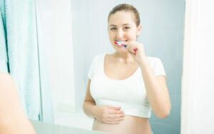 Pregnant woman brushing her teeth in the mirror