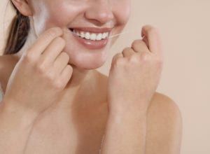 young woman uses dental floss to clean teeth